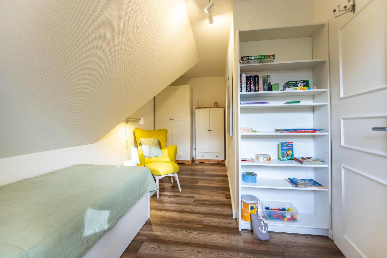 Schlafzimmer mit gelber Sitzgelegenheit, zwei weißen Schränken und Holzboden.