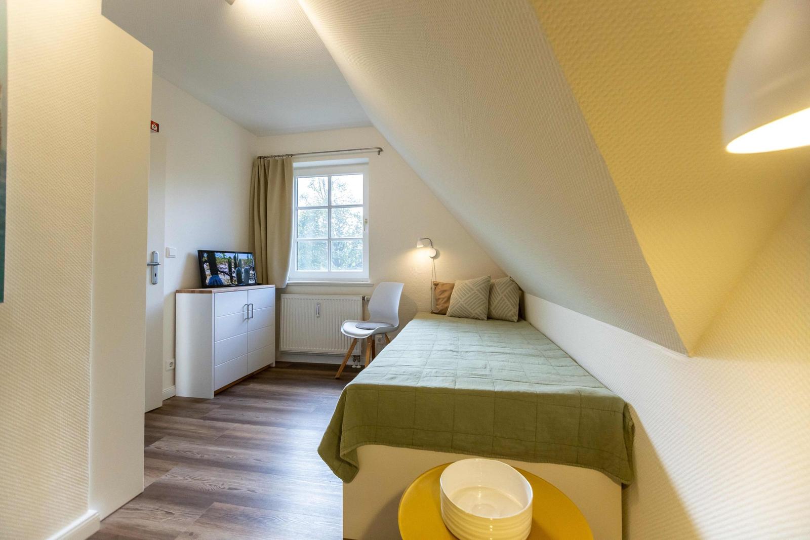 Schlafzimmer mit gelber Sitzgelegenheit, Bücherregal und Kleiderschränken unter Dachschrägen.