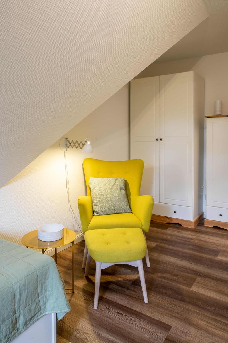 Ein Schlafzimmer mit Dachschräge, Bett, Stuhl, TV und Fenster mit Blick auf Bäume.