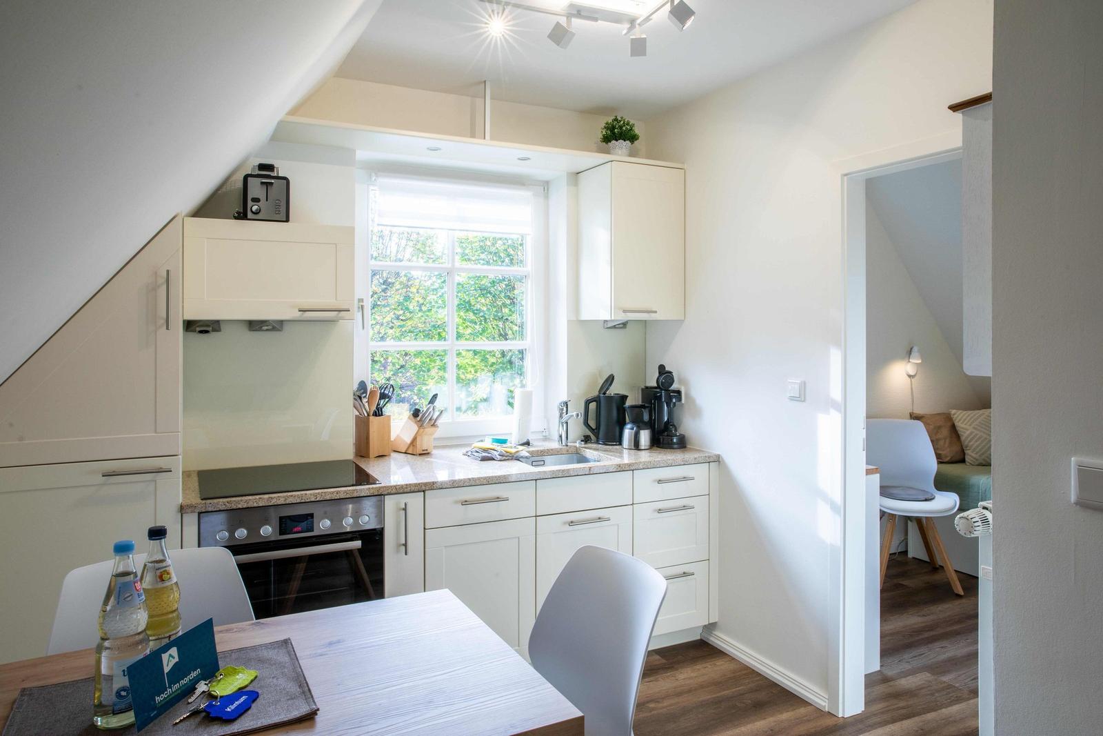 Küche mit Arbeitsplatte, Fenster und Essbereich mit Stühlen.