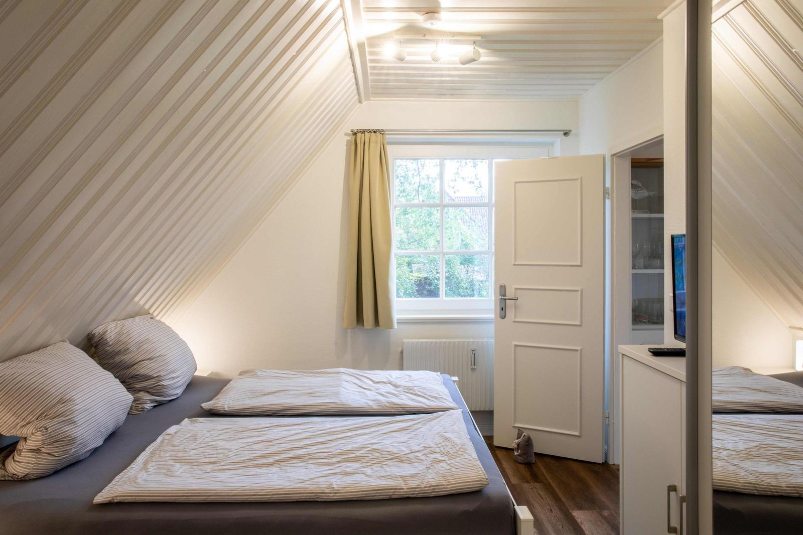 Zwei Betten mit gestreiften Kissen und Bettwäsche unter schrägem Dach mit Lampe.