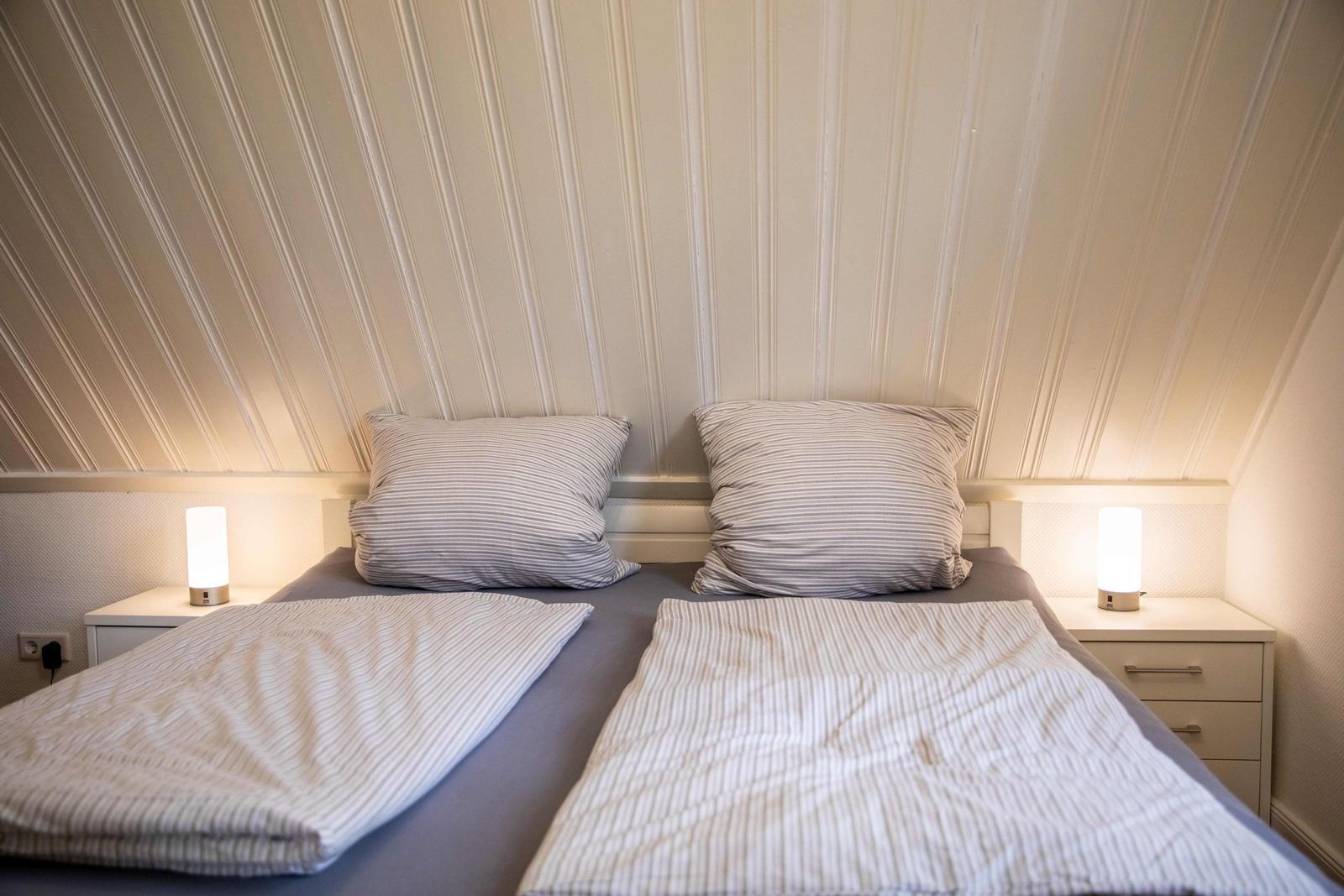 Wohnung mit Wohn- und Küchenbereich unter Dachschrägen, Sofa, Fernseher und Wandbild mit Leuchtturm.