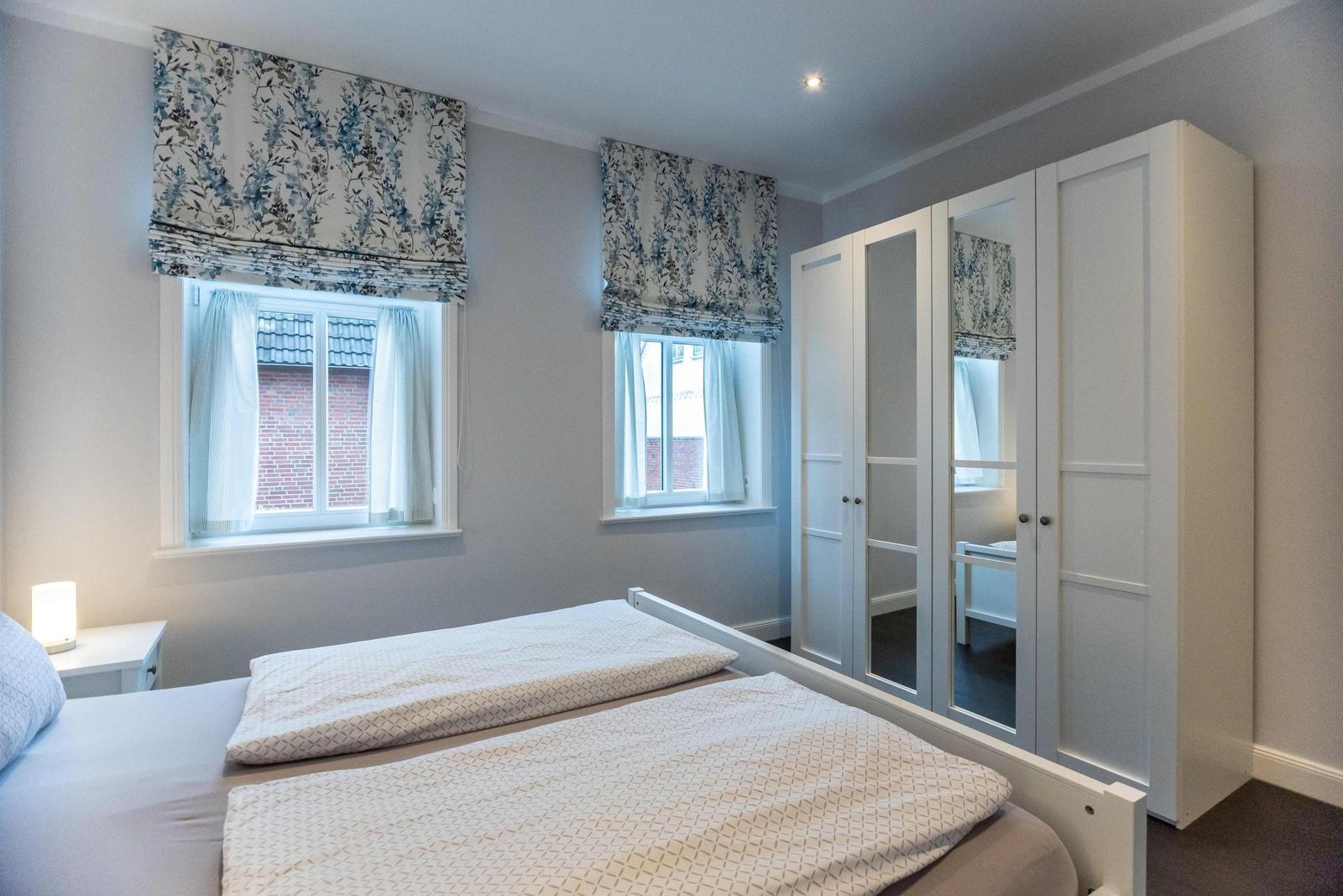 Bedroom with bed, nightstands, and TV. Window with floral roller blinds.