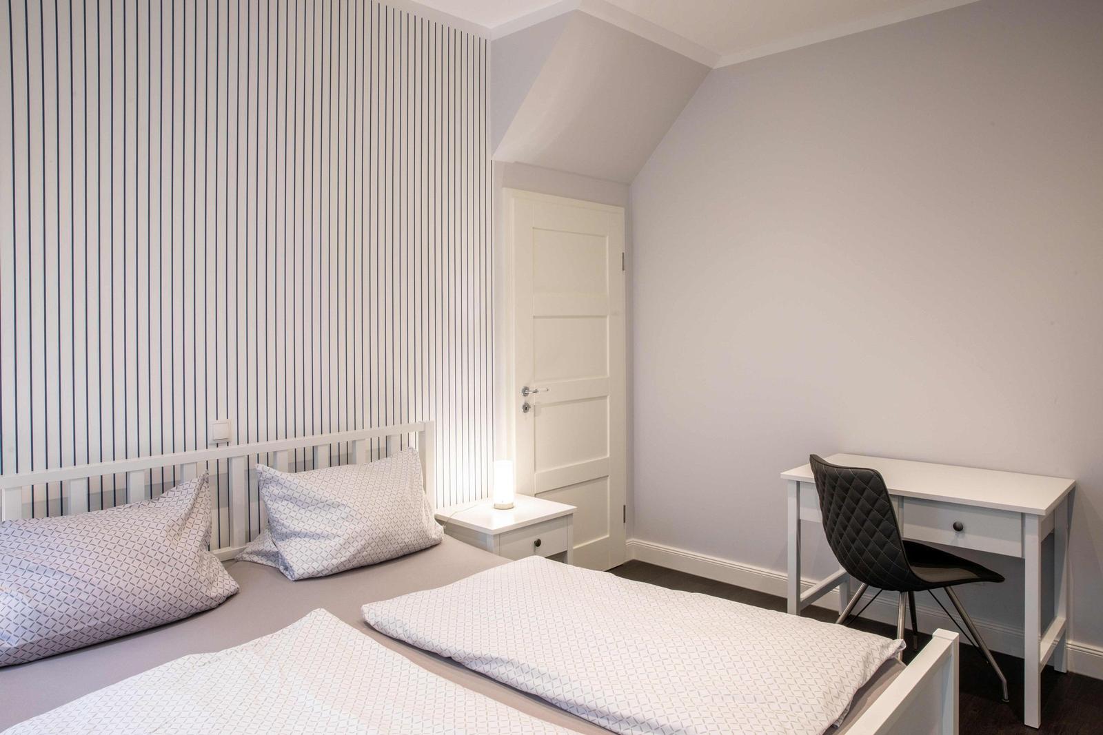 Bedroom with double bed, wardrobe, and view into living room with TV.