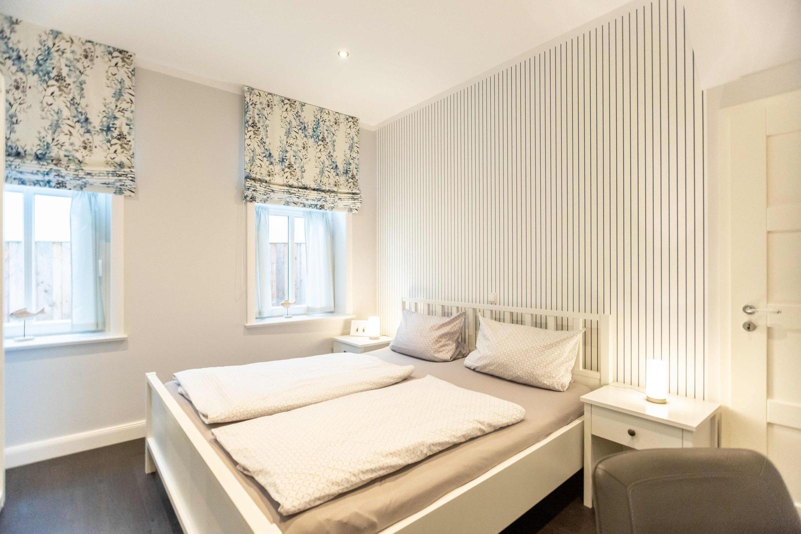Bedroom with double bed, two nightstands, and windows with blinds.