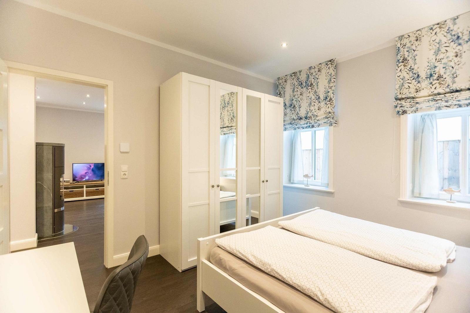 Bedroom with white bed, desk, and wardrobe with mirrored doors.