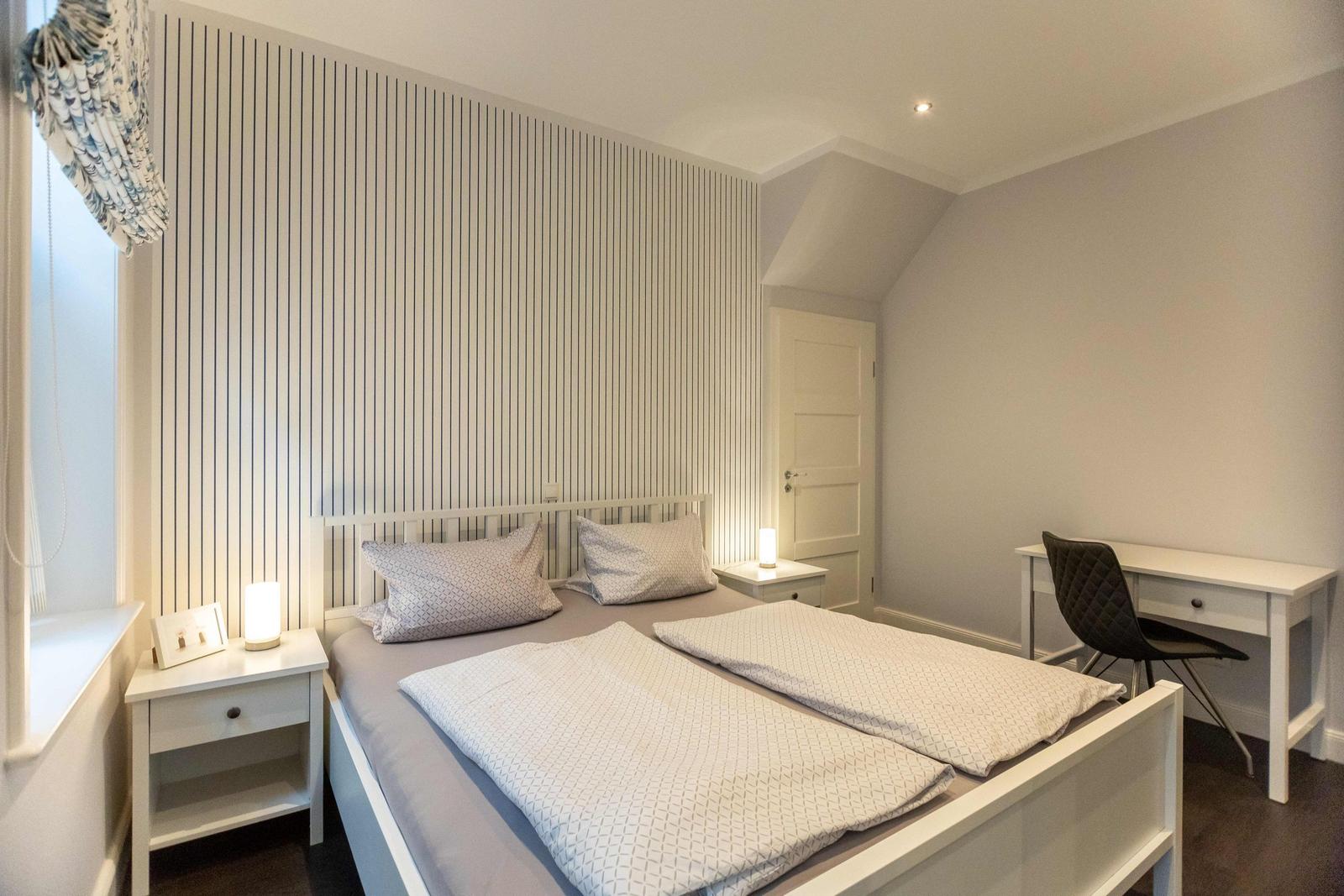 Bedroom with bed, wardrobe, and two windows with curtains.