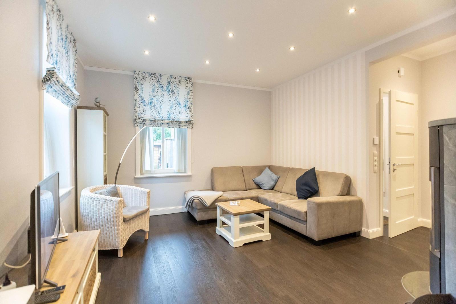 Living room with sofa, armchair, and table. Window with floral valance. Wooden floor and striped wall.