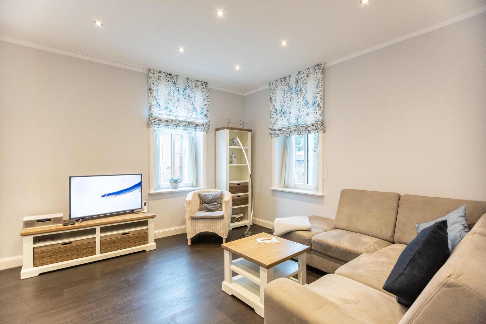 Living room with sofa, TV, and two windows with floral roller blinds.
