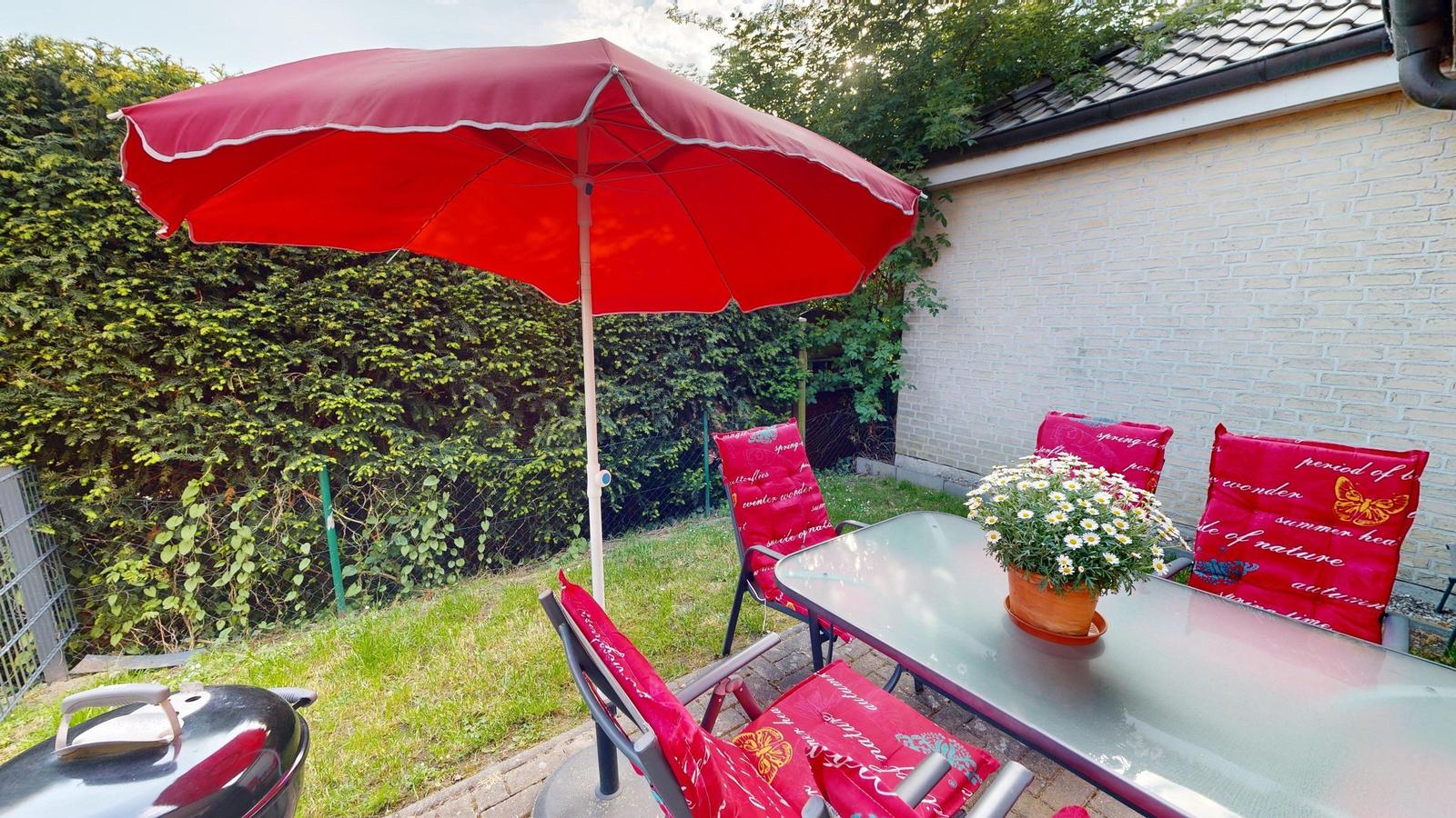 Wohnzimmer mit Sofa, Fernseher und Blick auf den Garten mit Sonnenschirm.