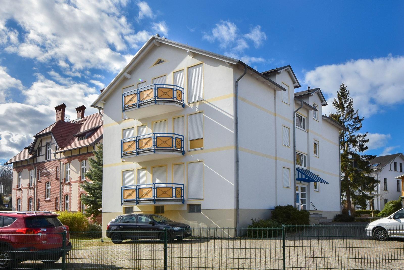 Ein mehrstöckiges Haus mit Balkonen und Gartenbereich unter blauem Himmel.