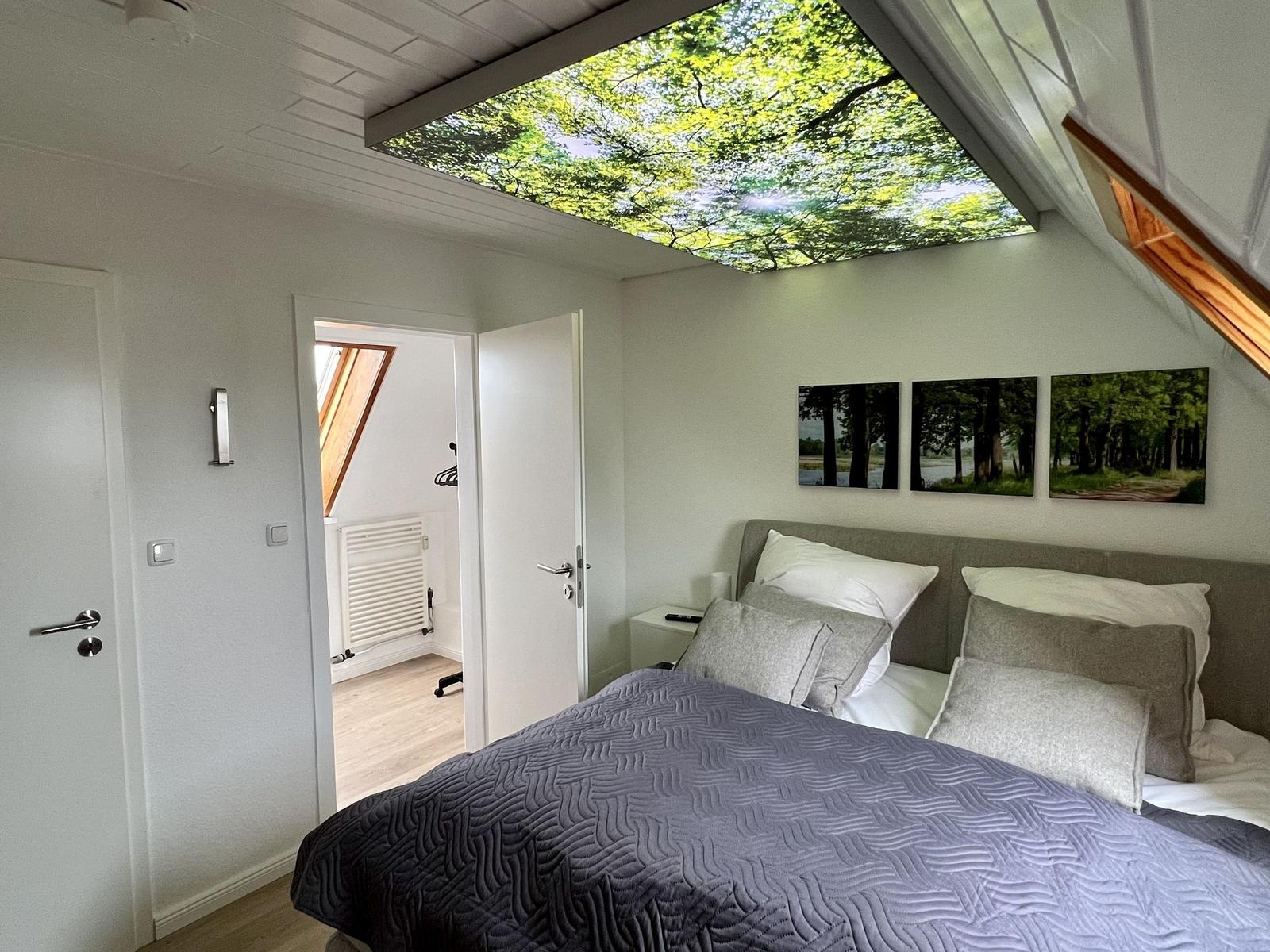 Ein Schlafzimmer mit Dachschräge, Bett und Wandbild.
