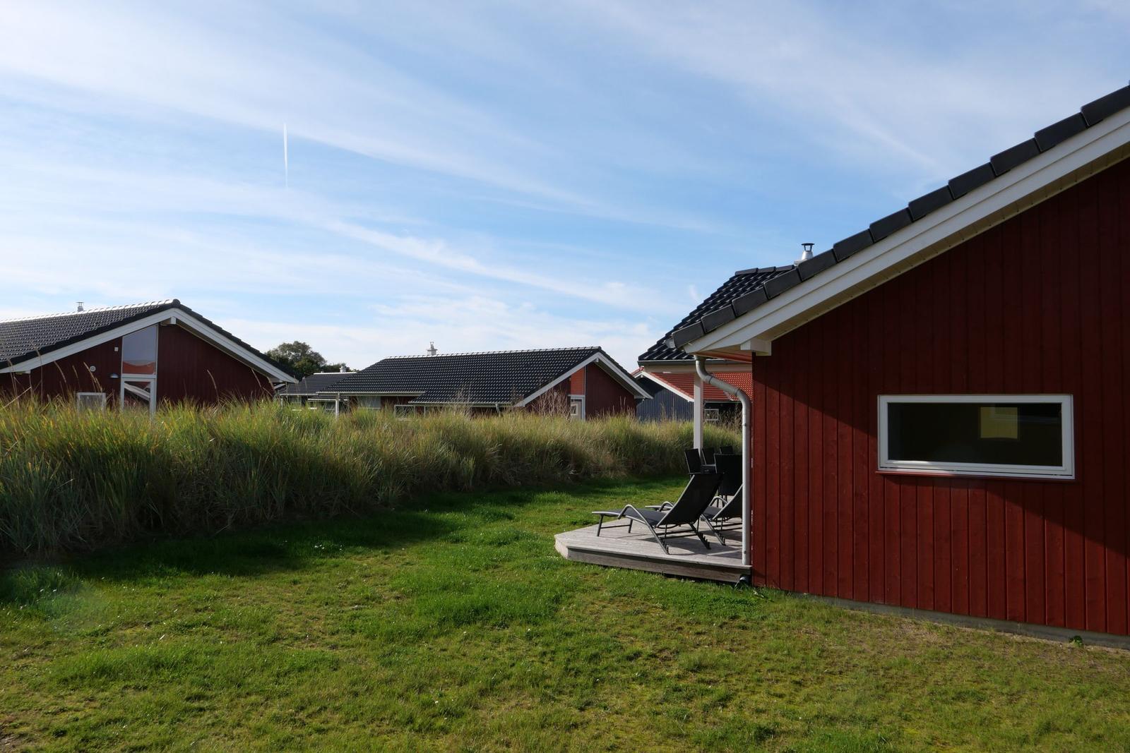 Rotes Ferienhaus mit Terrasse und Garten. Schwarzer Dachfirst und weiße Fensterrahmen.
