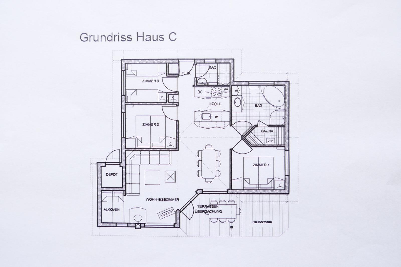 Rotes Haus mit Terrasse und Garten. Große Fenster und schwarze Dachziegel.