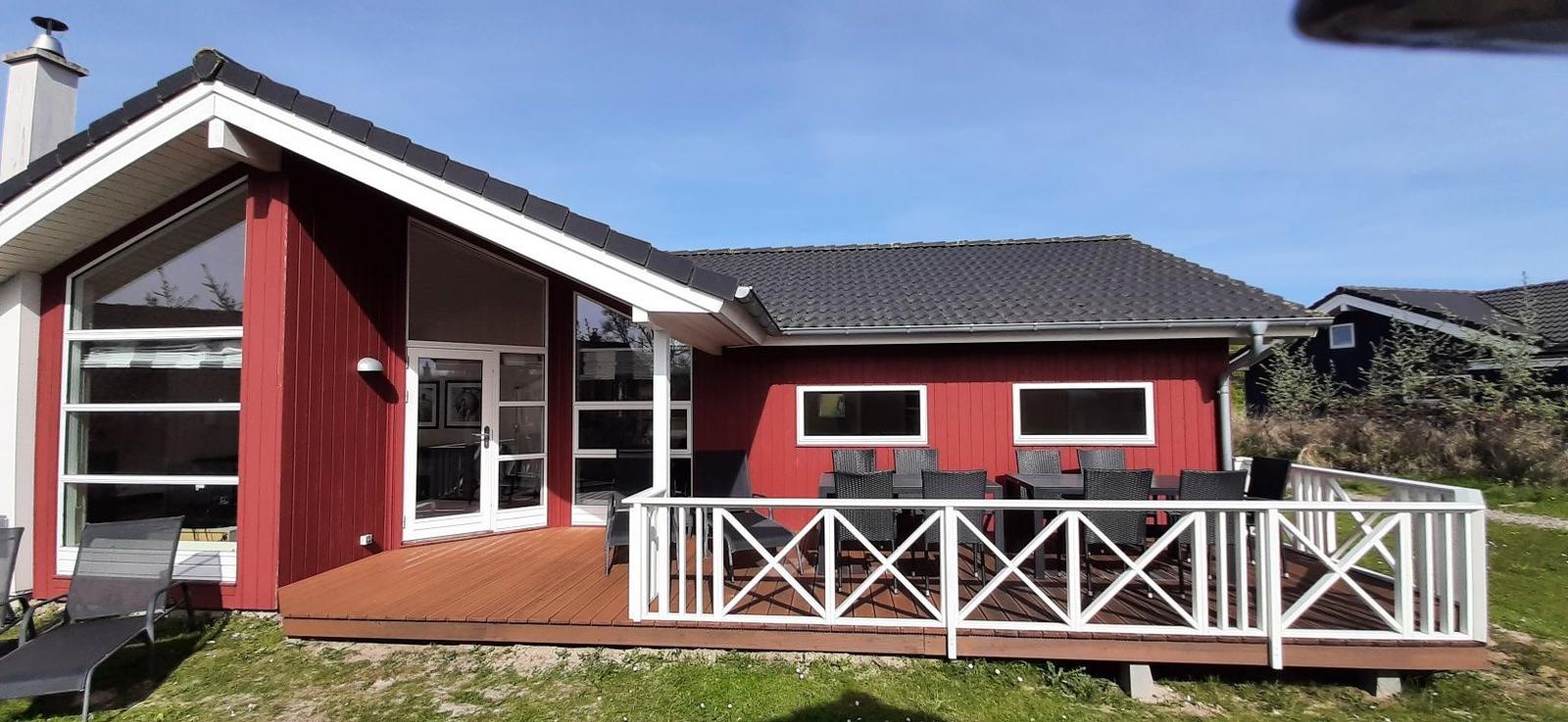 Rotes Haus mit Terrasse, Garten und Sitzgelegenheiten.