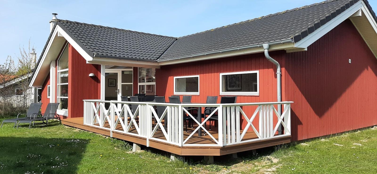Rotes Ferienhaus mit Terrasse und Garten. Sicht auf Eingang und Fensterfront.