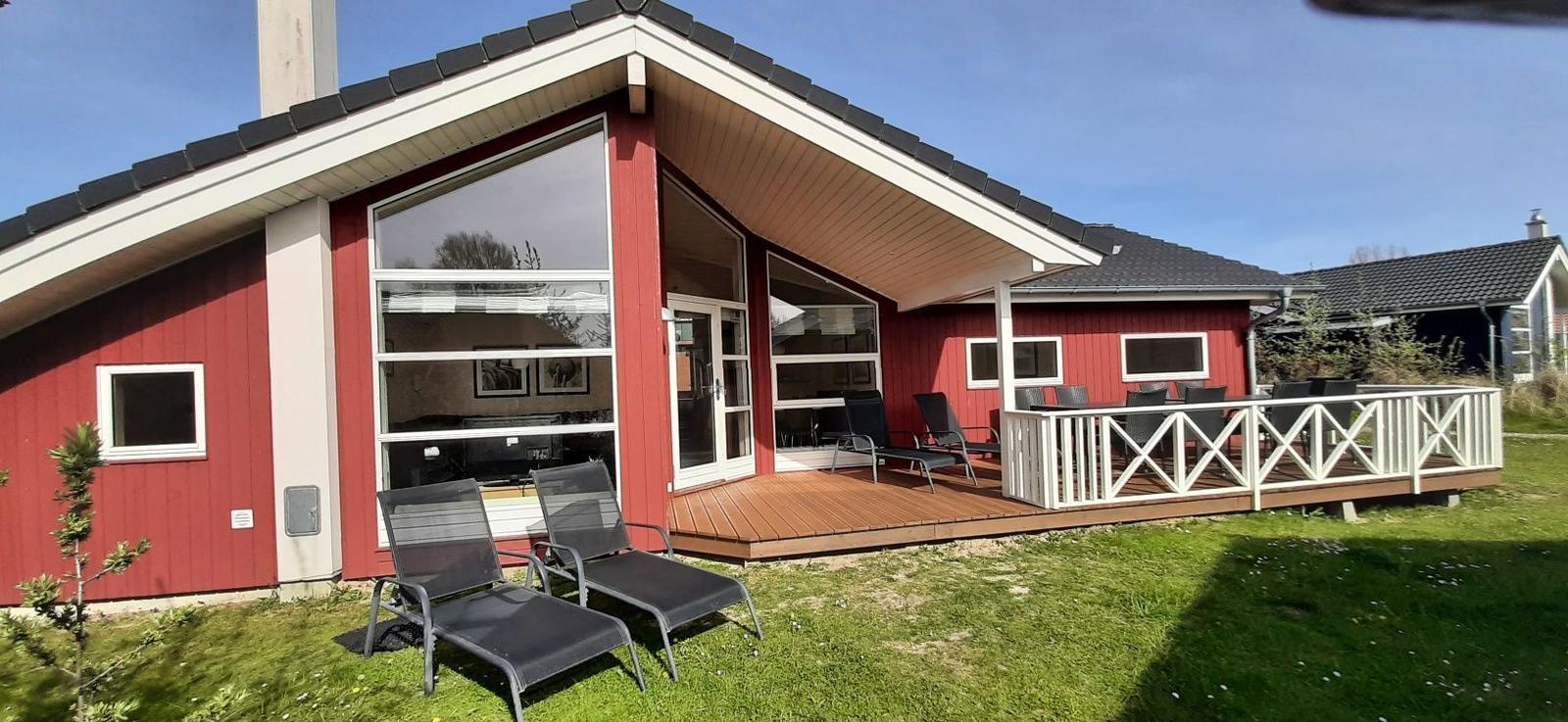 Rotes Ferienhaus mit Terrasse und Garten. Sicht auf die Eingangstüren und Fenster.