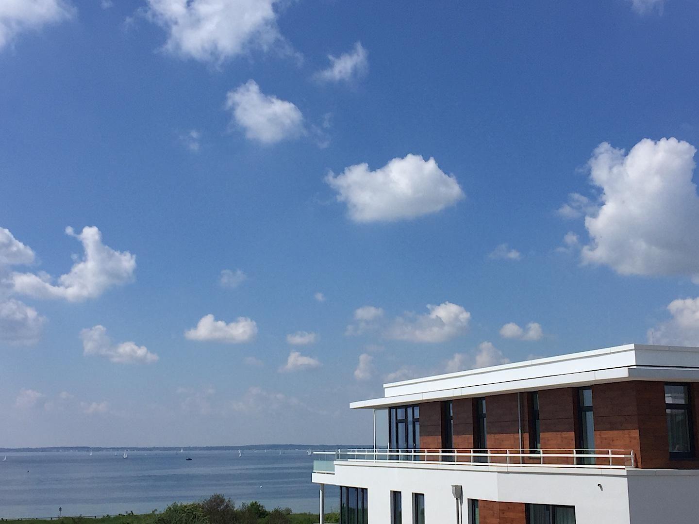 Strand mit Dünen und modernen Ferienhäusern im Hintergrund.