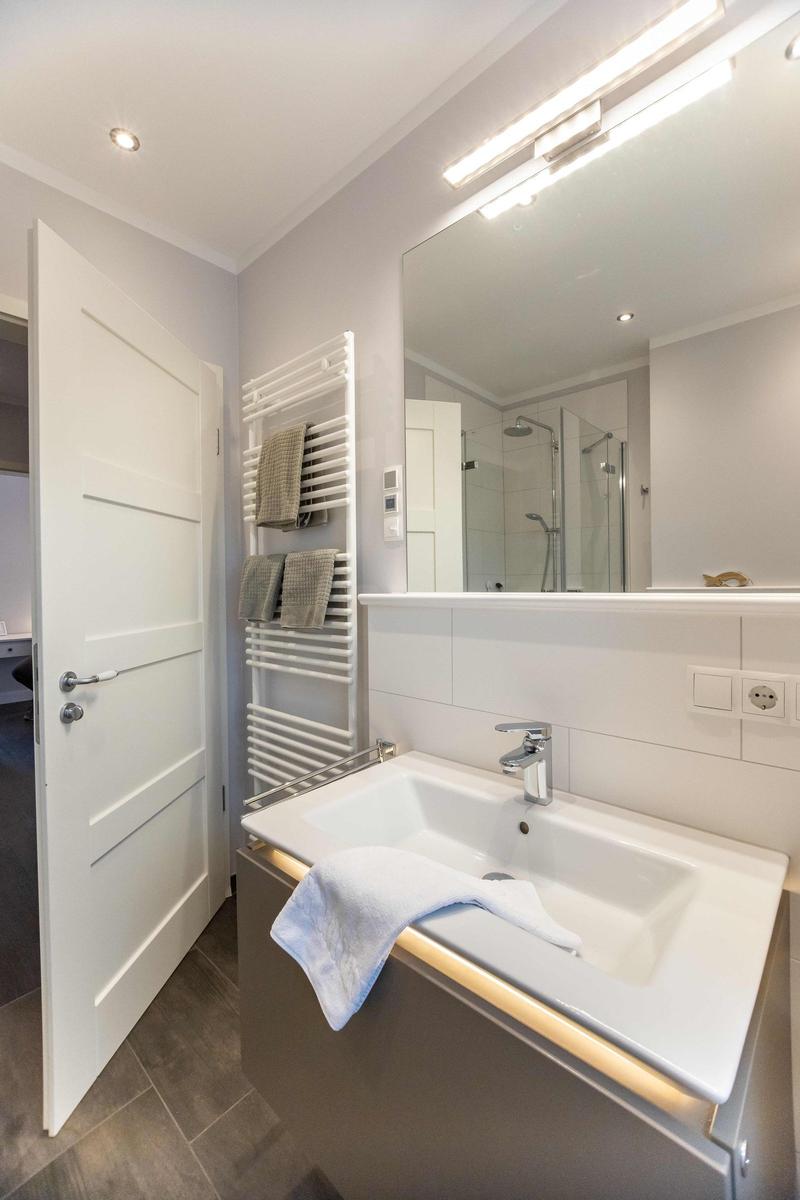 Badezimmer mit Waschbecken, WC und Dusche. Fenster mit Blumenvorhang und weißen Vorhängen.