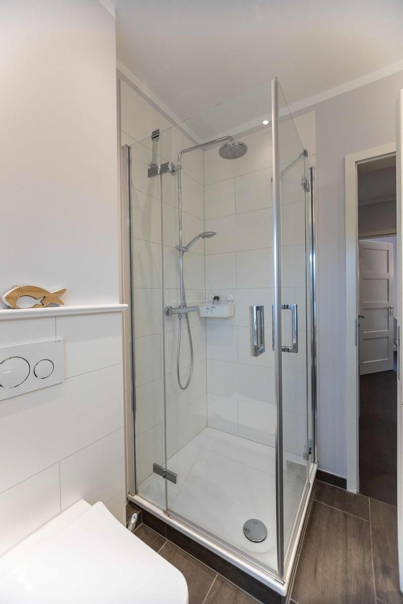 Duschkabine mit Glaswand, Toilette und Fenster mit Vorhang.