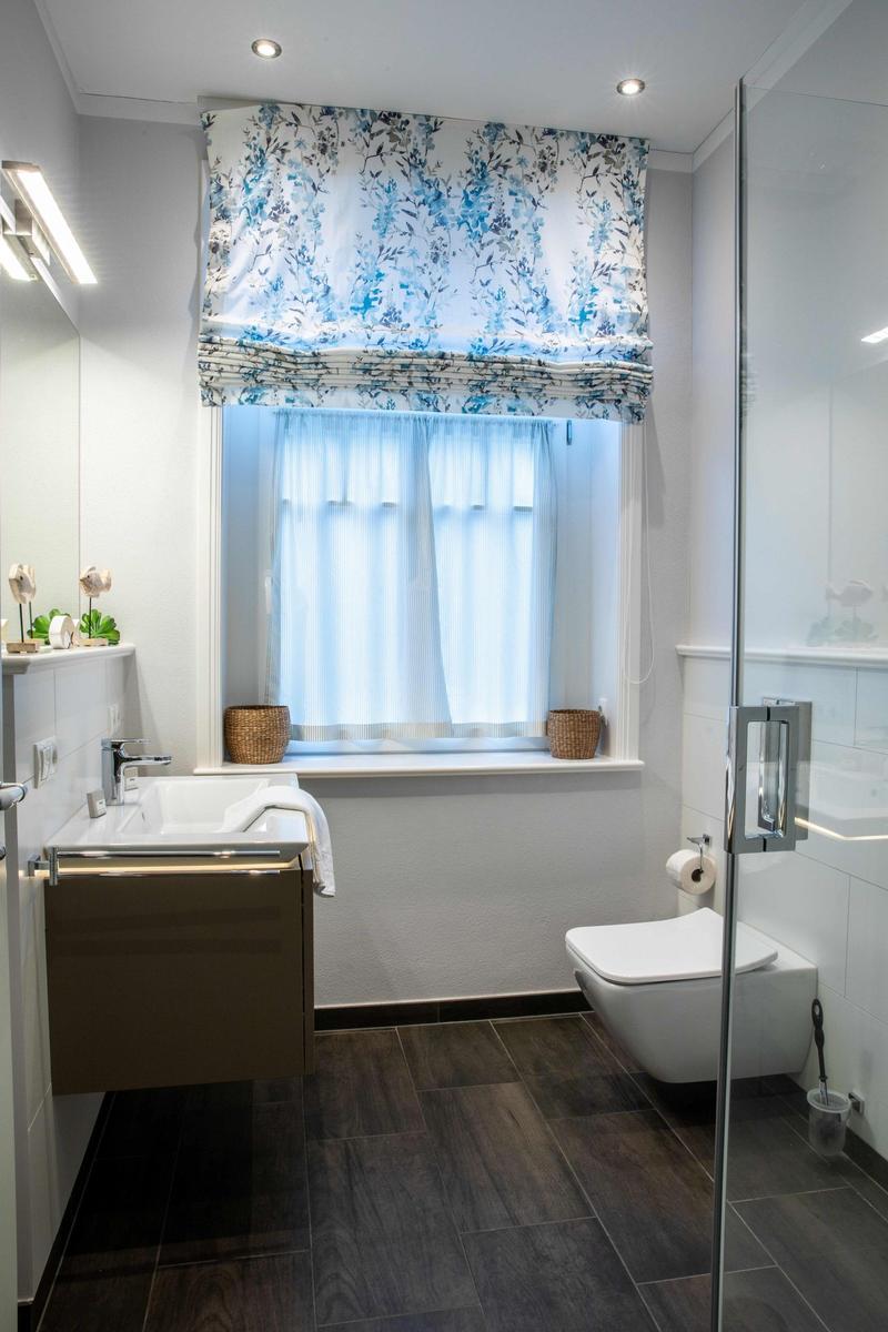 Badezimmer mit Waschbecken, Toilette und Fenster mit Vorhängen.