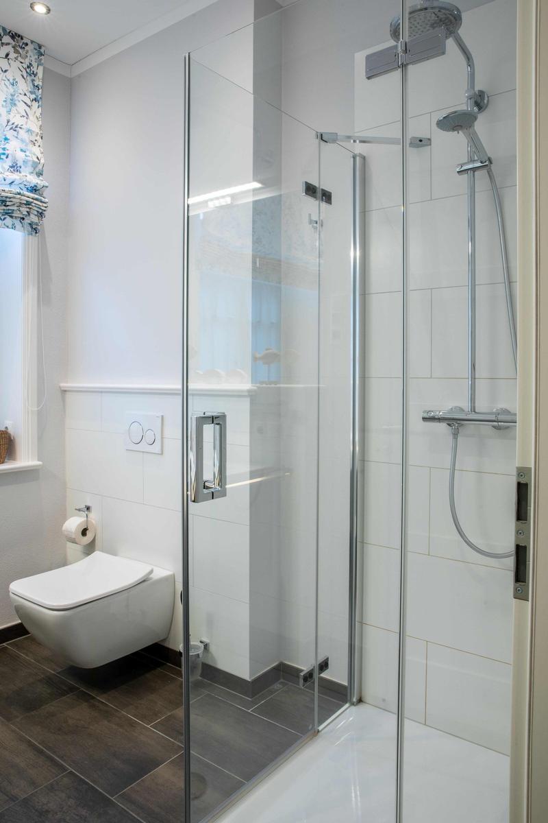 Badezimmer mit Dusche, Toilette und Fenster mit Vorhängen.