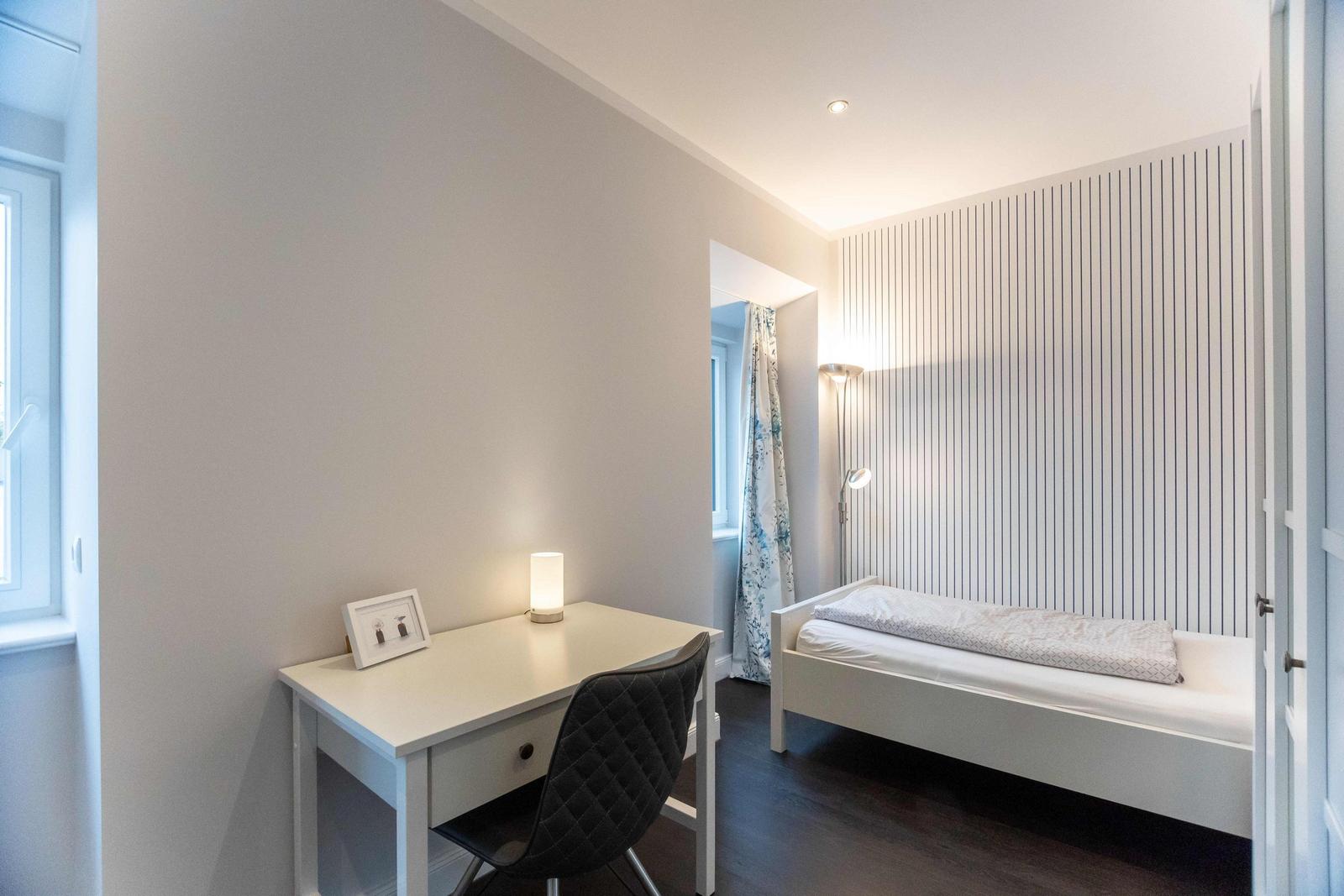 Schlafzimmer mit Schrank, Schreibtisch und Bett. Hinter Tür weitere Schlafgelegenheit.