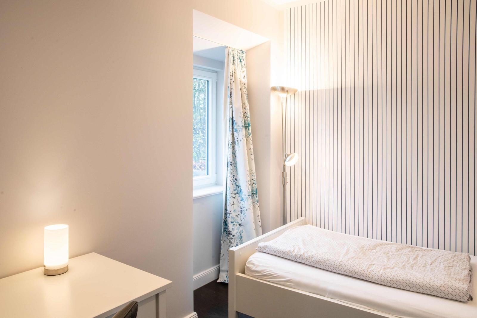 Schlafzimmer mit Bett, Schreibtisch und Kleiderschrank. Wand mit vertikalen Streifen.