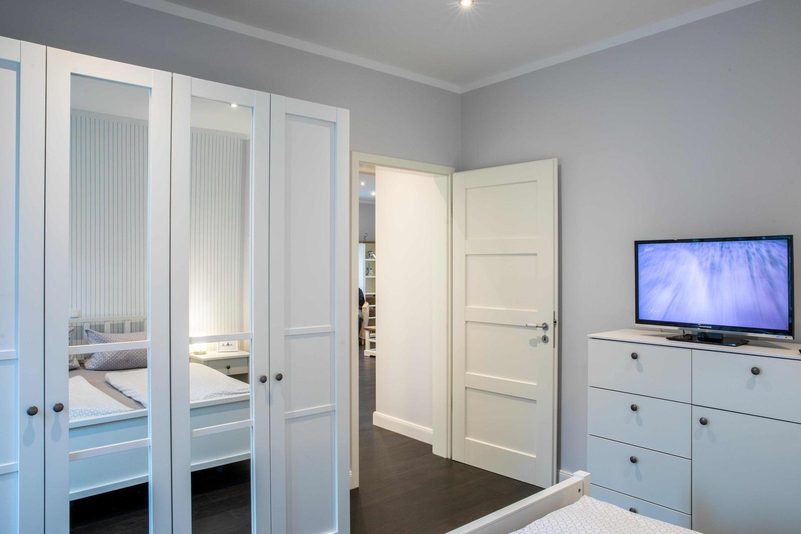Schlafzimmer mit Bett, Kleiderschrank und vertikaler Wandverkleidung.
