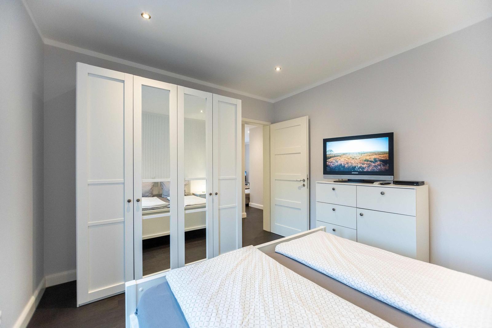 Schlafzimmer mit Doppelbett, weißen Schränken und Fenster mit Rollladen.
