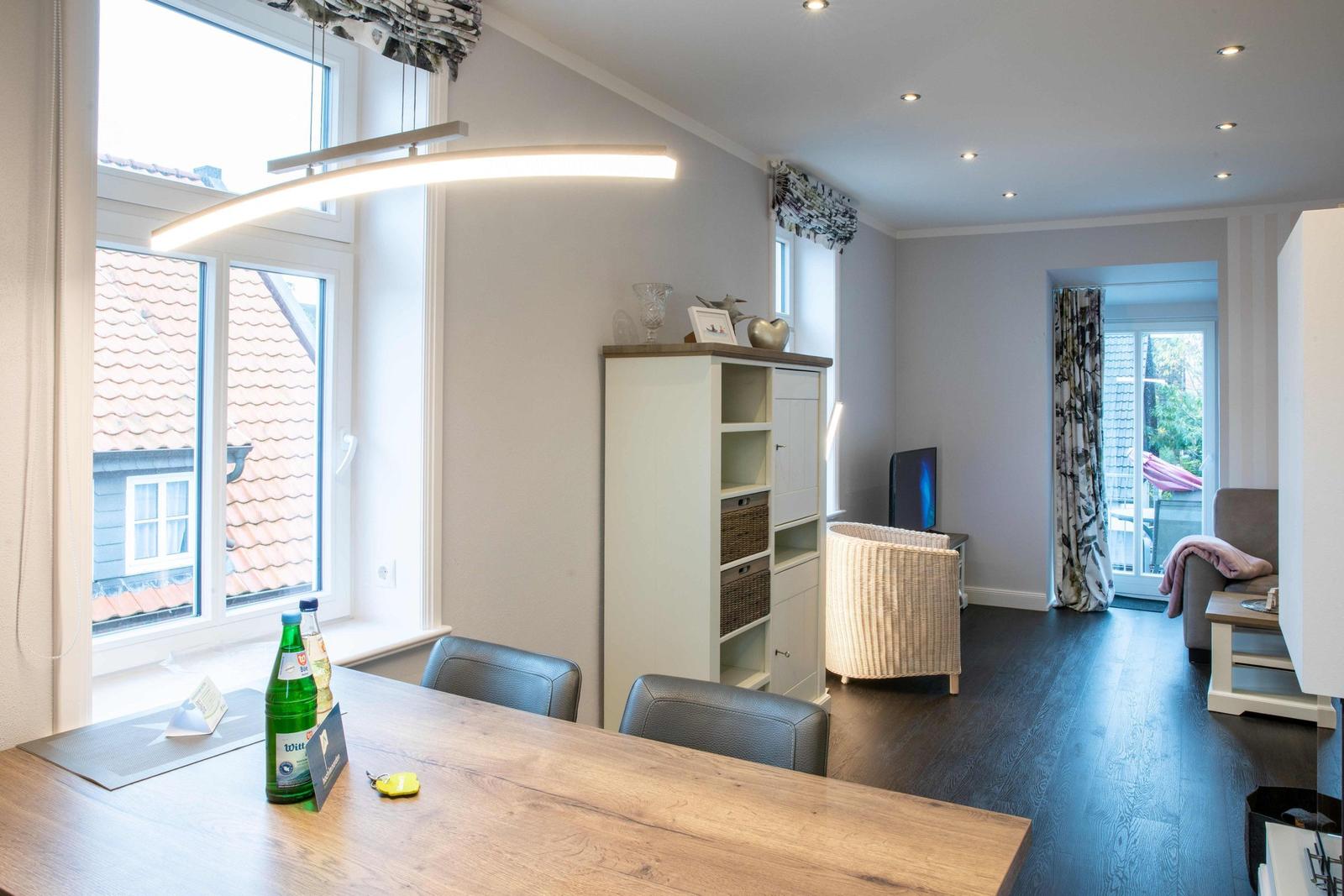Wohnzimmer mit Sofa, Fernseher und Sideboard. Holzboden und Fenster mit Vorhängen.