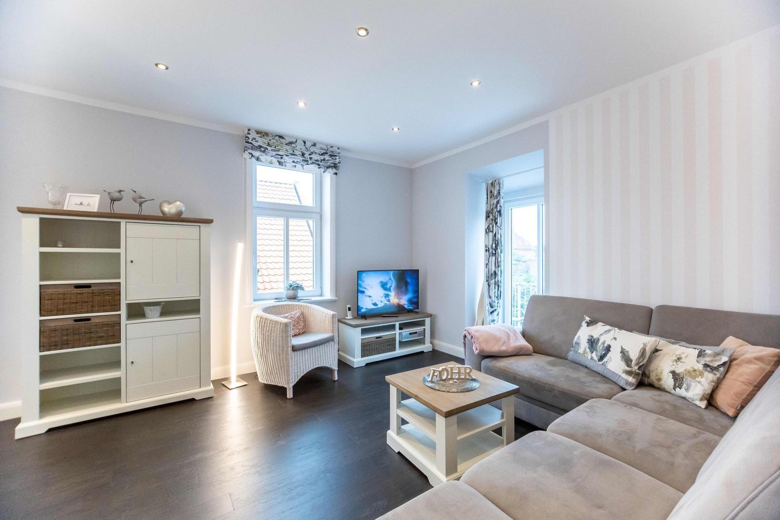Wohnzimmer mit Sofa, Sessel, Fernseher und Fenstern.