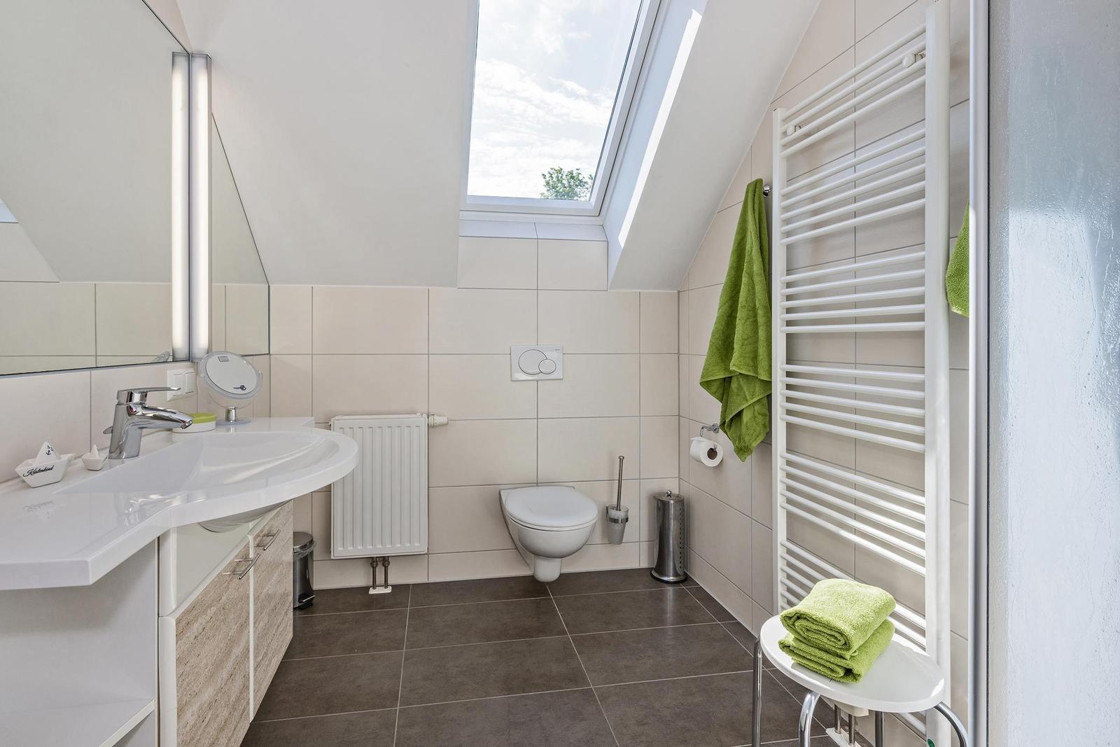Badezimmer mit Dusche, Waschbecken und Toilette unter Dachschrägen.