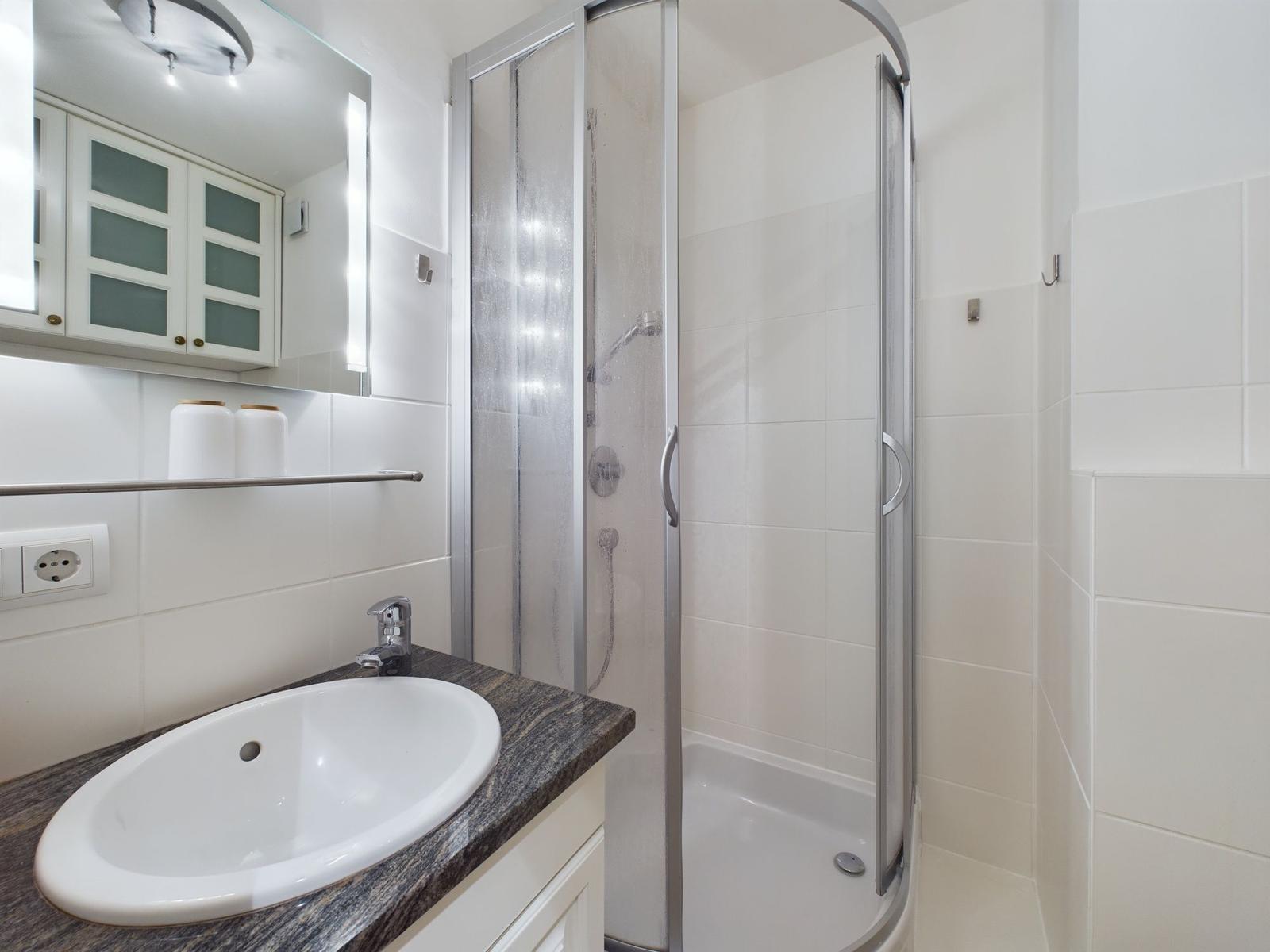 Badezimmer mit Dusche, WC und weißen Fliesen.