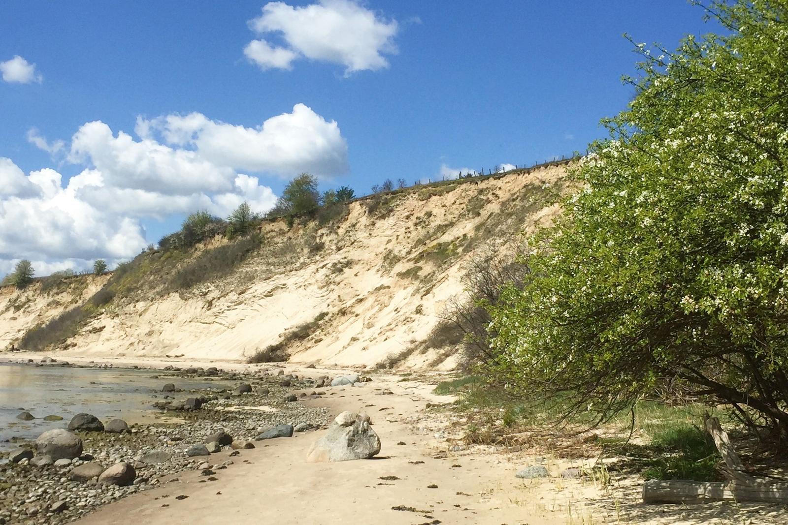 Holzsteg führt zum Meer, Schiff fährt vorbei unter blauem Himmel mit weißen Wolken.