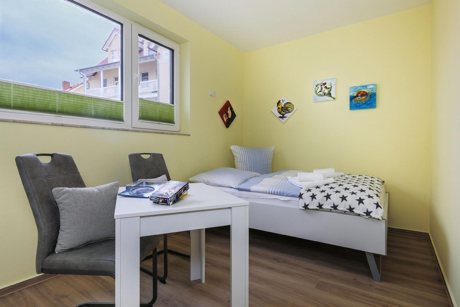 Ein Raum mit weißem Schreibtisch, Stuhl und Kleiderschrank an der Wand.