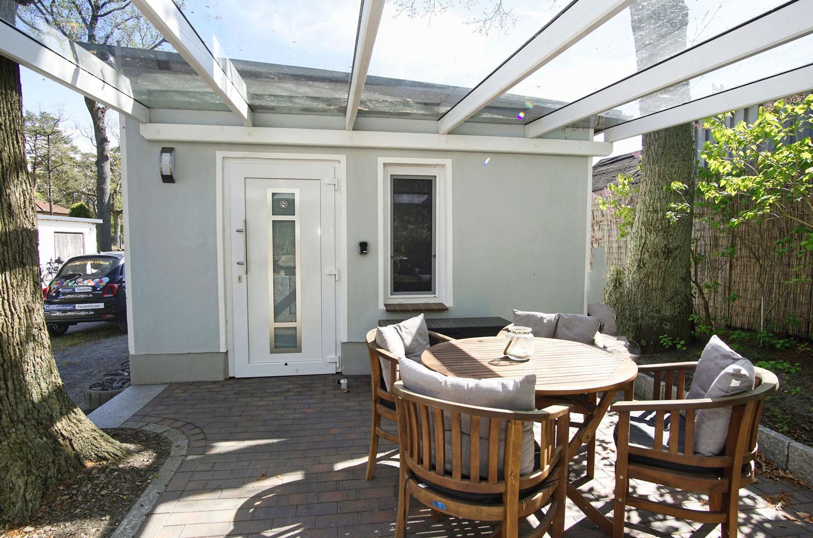 Wohnhaus mit Terrasse, Sonnenschirm und Tisch. Hinterhof mit Bäumen und gepflastertem Weg.