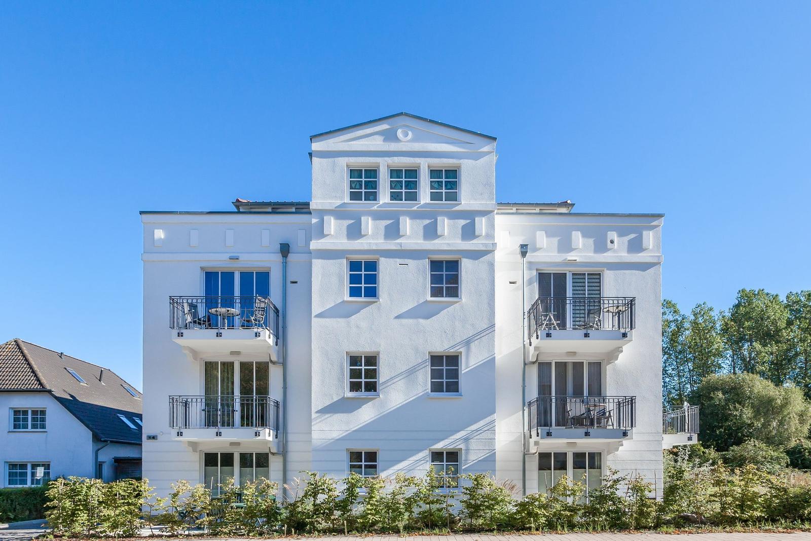 Weißes Mehrfamilienhaus mit Balkonen und Fenstern unter blauem Himmel.