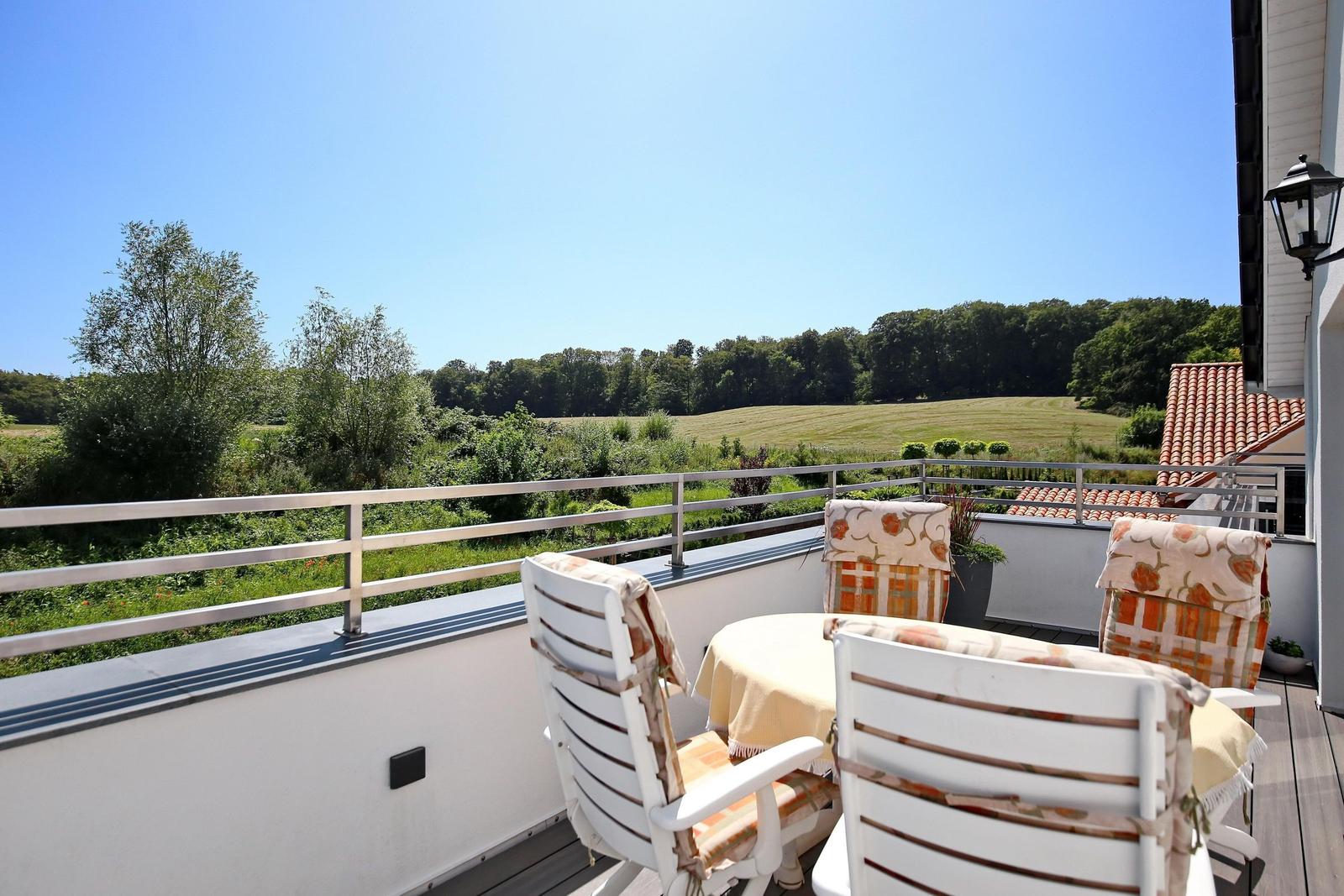 Moderne weiße Villa mit Terrasse, Garten und Poolbereich unter blauem Himmel.