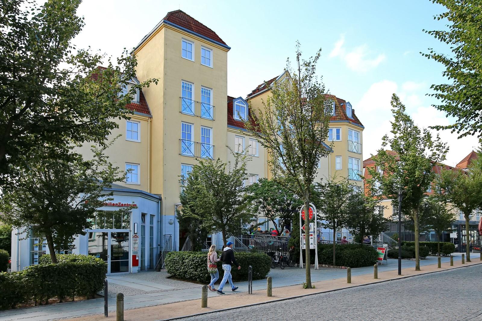 Gelbes Gebäude mit rotem Dach und Bäumen im Vordergrund.