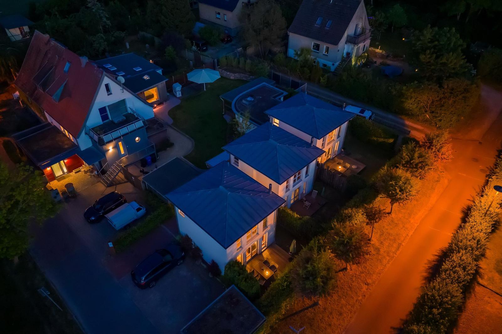 Nachtansicht von mehreren Häusern mit beleuchteten Fenstern und Gartenbereichen.