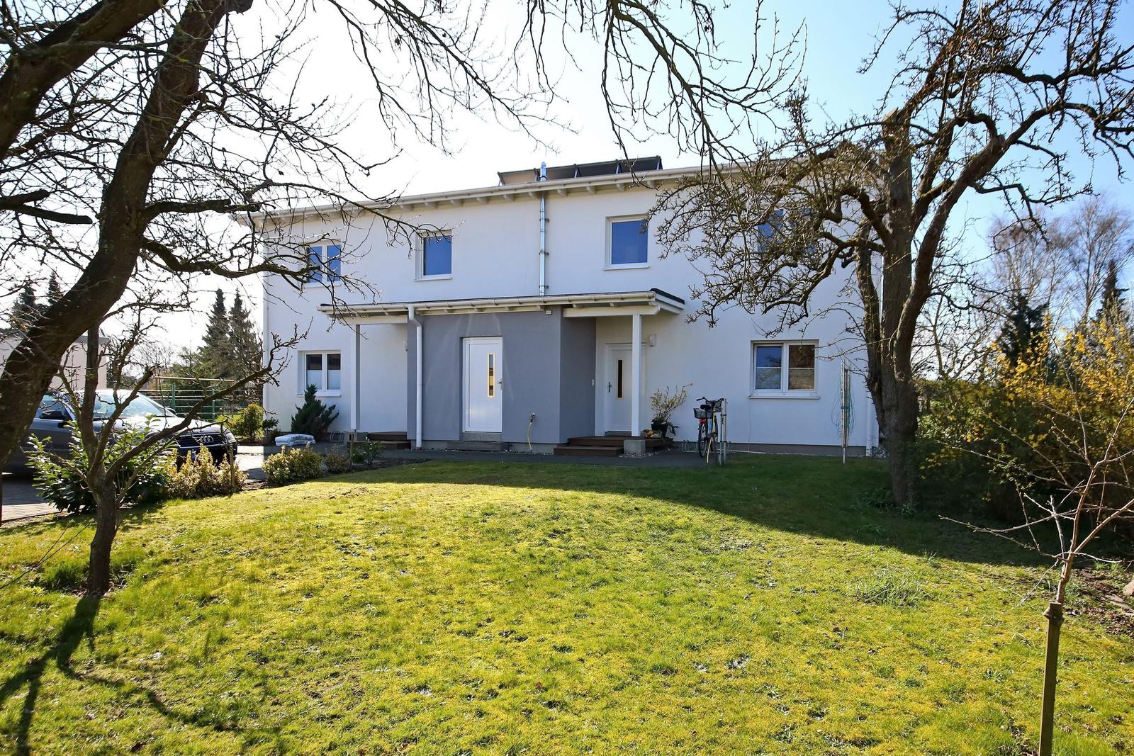 Moderne weiße Villa mit Garten und Bäumen. Eingangstür und Fenster sichtbar.
