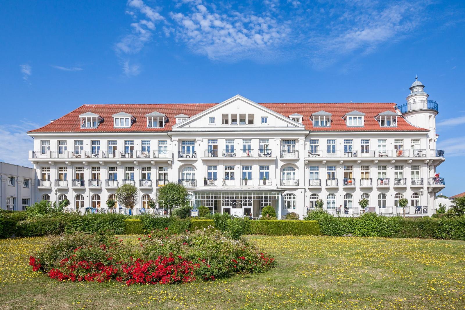 Weißes Gebäude mit rotem Dach, Balkonen und Garten vorne.