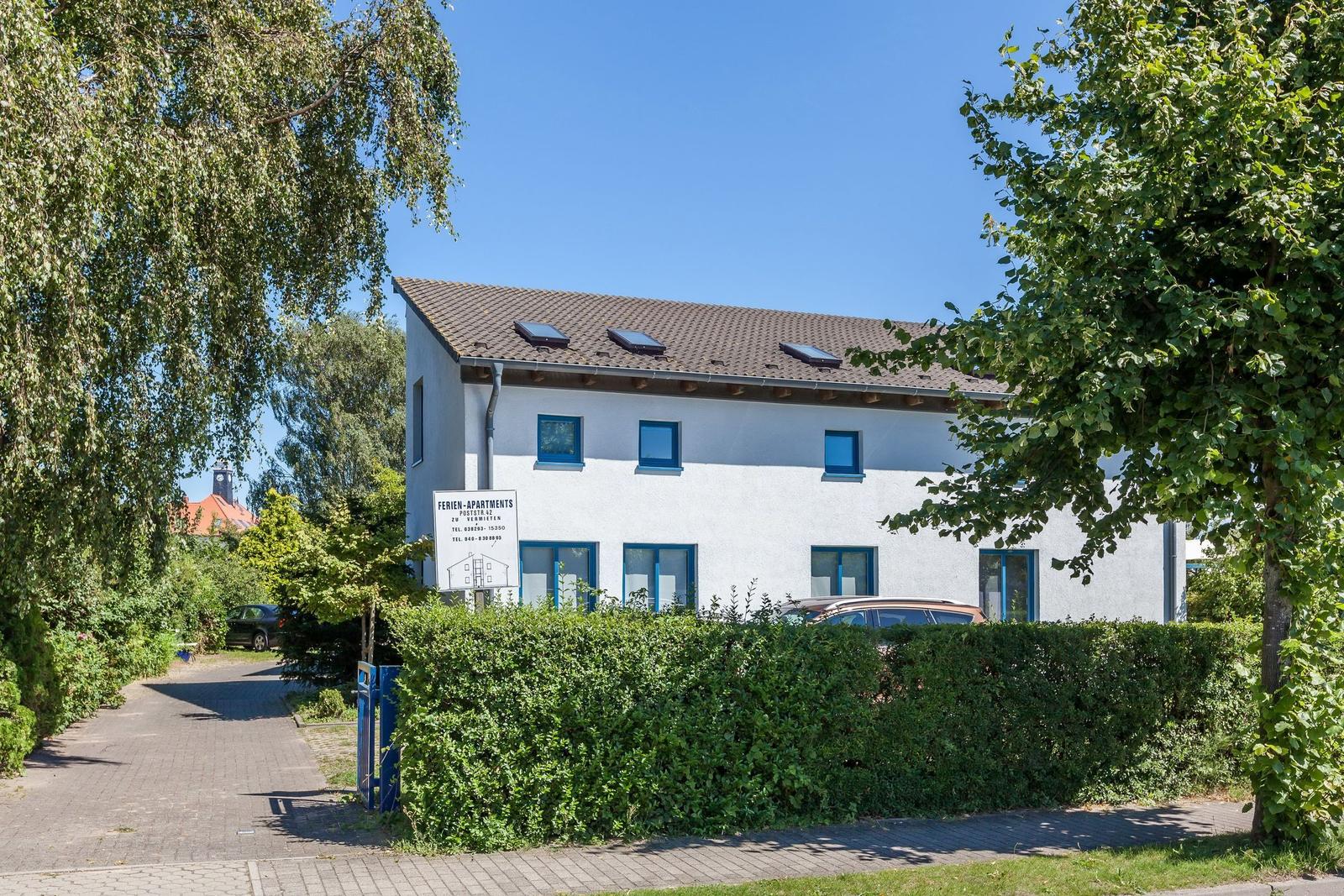 Ferien-Apartments mit blauen Fenstern und Dachfenstern, umgeben von Bäumen und Hecken.