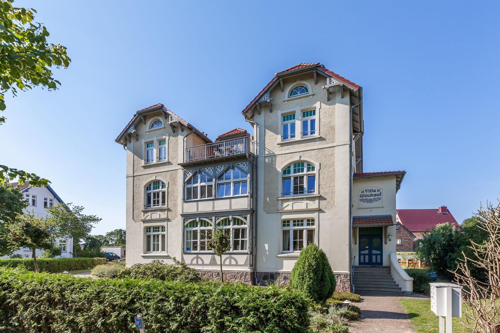 Villa Glückauf mit Balkon und gepflegtem Garten unter blauem Himmel.