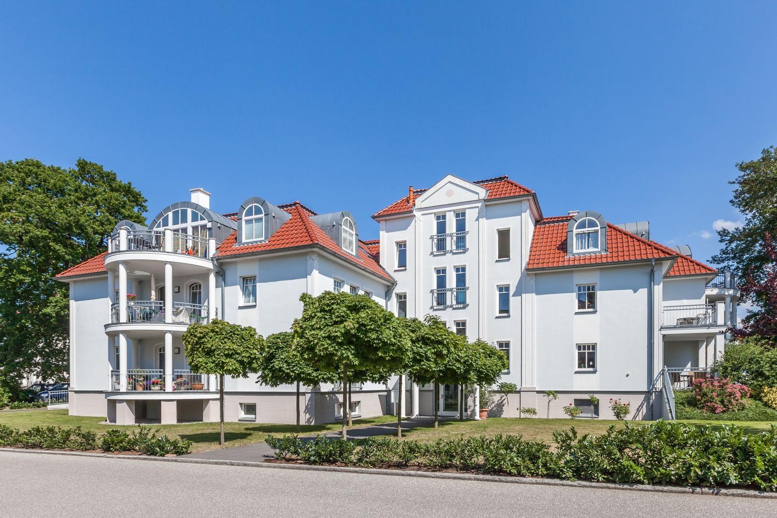 Weiße Villa mit rotem Dach und Balkonen. Grün umgeben. Ideal für Urlaub.