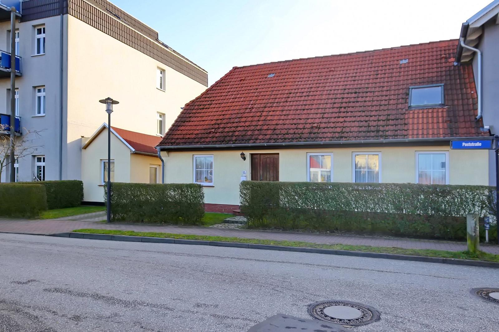 Ein gelbes Haus mit rotem Dach und grüner Hecke an der Straße.