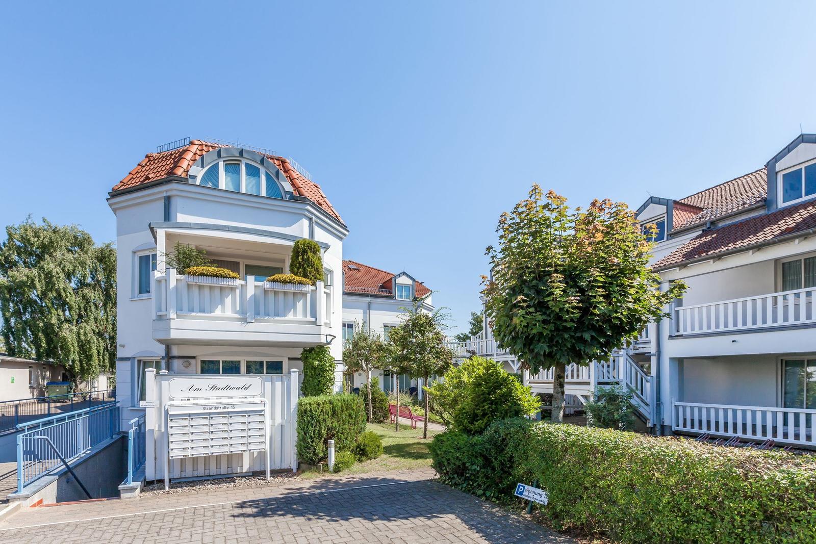 Wohnhaus mit Balkon, rotem Dach und Gartenbereich. Sichtbarer Briefkasten und Parkplatz.