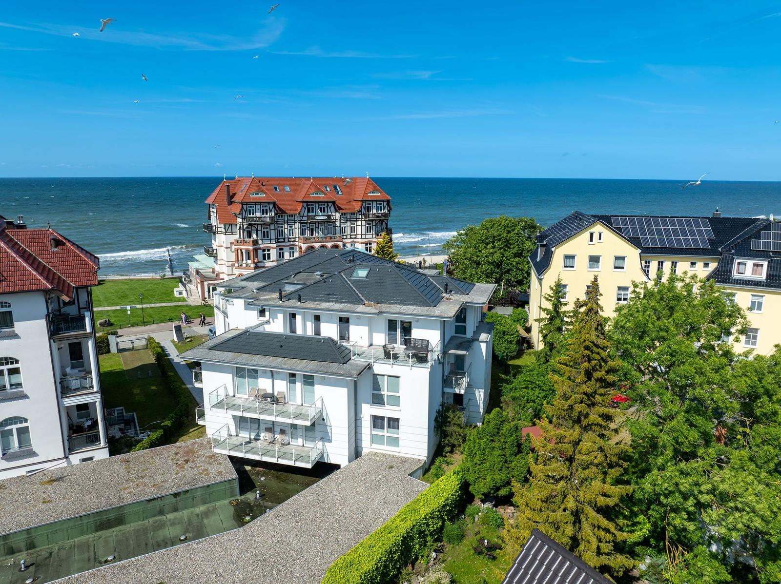 Meerblick auf mehrere Häuser mit Terrassen und grünen Bäumen an der Küste.