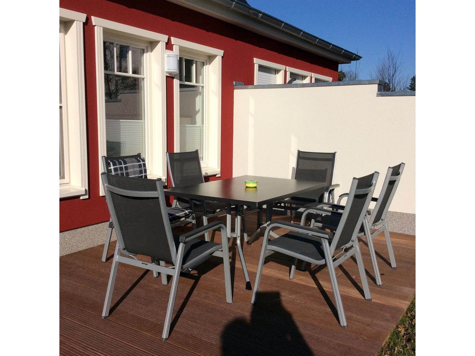 Rotes Haus mit Holzterrasse und grünem Garten. Dach mit Satellitenschüsseln und Dachfenstern.